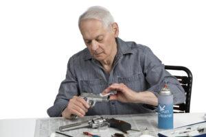 senior man sitting while looking down and cleaning stainless steel hand gun on table