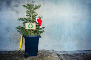 small Christmas tree topped with red santa hat thrown into a recycle trash bin after celebrations