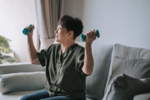 older woman of Asian descent exercising with 2 lb weights in her home