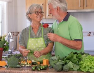 Senior couple cooking in the kitchen looking at each other tenderly husband offers a rose to wife