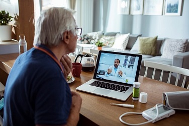 senior man sitting at laptop participating in telehealth doctor appointment
