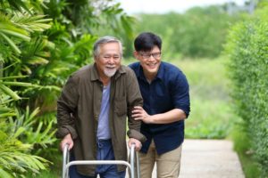 Happy elder Asian man using walker while walking for exercise around the garden with his son walks with him