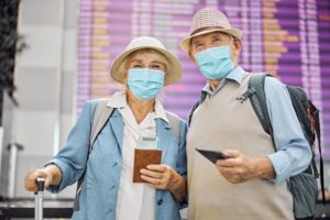 Two older Caucasian travelers in protective masks holding their passports and boarding tickets