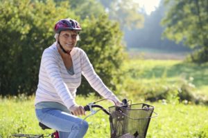 older adult woman riding her bike through lush green nature scene